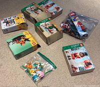 Photo showing various LEGO holiday-themed boxes and loose pieces on carpeted floor, including Halloween pumpkin set and Christmas character sets, some boxed, some open with contents in zip bags.