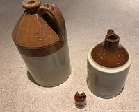 Three stoneware jugs displayed upright: a large Medalta jug, a medium British Doulton jug, and a small reddish-brown Randolff Alberta jug