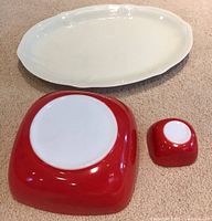 Set of three items shown on carpet: large white ceramic platter and two red Pyrex bowls (large chip and small dip).