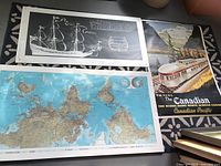 Photo shows three items: top black and white ship drawing, bottom large world map, right side Canadian train travel poster.