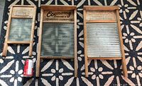 Photo of three vintage washboards laid on patterned floor with soda can for scale; left is National glass washboard, center Economy Canadian Woodenware Co. glass washboard, right metal corrugated Western Brand washboard.