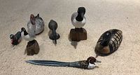Five small carved wood duck figurines and one decorative letter opener with a bird head handle arranged on carpet.