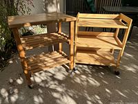 Pair of wooden rolling carts displayed outdoors with sunlight and shadows, showing overall structure and condition.