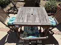 Top down view of the square wood outdoor table with 4 chairs around it, showing cushion patterns and table slats.
