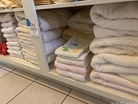 Shelf stacked with mostly white bath towels, bath sheets, and small towel items, including multicolored holiday decorative hand towels with embroidered designs.