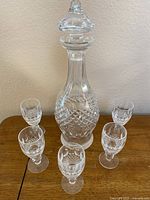 Full view of Waterford crystal decanter with stopper surrounded by five short stem claret wine glasses on a wood surface.
