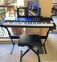 Full view of Donner DEK-610 keyboard on the adjustable stand with bench stool, piano book placed on music stand, and microphone on right speaker.