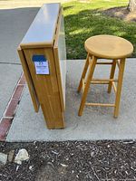 Folded table with two sides down, wooden stool next to it, showing the compactness when folded.