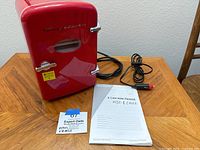 Frigidaire mini fridge with power cord, small size to hold six cans, user manual and a note card visible on table.