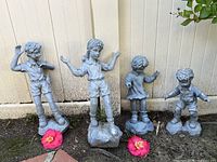 Four clay garden kid statues in a row against the fence with two flowers placed in front