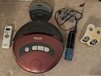 Full view of the Roomba vacuum with remote, charger, cleaning brush tool, and batteries on carpeted floor.