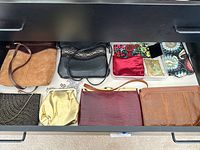 Drawer with 9 handbags including brown leather, black leather, tan suede, beaded clutch bags, and patterned fabric bags arranged side by side.