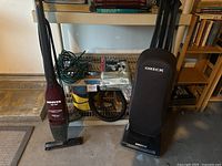 Photo showing Hoover Sprint handheld vacuum, Oreck upright vacuum, Stinger wet dry vacuum hose and accessories on shelf