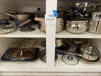 Upper and lower shelves with assorted pots, saucepans, frying pans, and lids in white shelving unit.