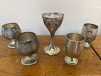 Five sterling silver mini cordial cups arranged on wooden surface: two rounded Gorham cups, two similar B&M cups, and one taller crimped cup in middle