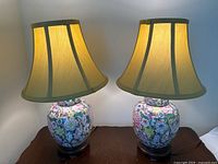 Two Asian style table lamps on a wooden surface showing overall appearance with beige shades and floral ceramic bases.