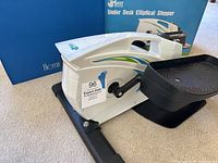 Photo showing the elliptical stepper with side view, displaying the body, pedal, and part of the box behind it.