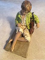 Full front view of the seated sleeping boy holding a violin and bow on a rectangular base.