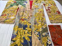 Full view of the vintage Japanese silk kimono laid flat showing the detailed yellow leaf motifs and red floral accents, as well as the obi belt at the edge.
