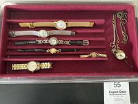 Seven women's watches diverse in style with a red holder tray and a pendant watch with chain.