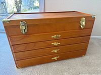 Closed wood jewelry storage box with warm natural finish, metal latch locks and decorative drawer handles.