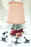 Red wooden airplane lamp with burlap shade beside four black high gloss ceramic Spitfire airplanes with white circle insignia, all on a white fabric background.