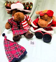 Photo showing two plush moose dolls, Hal on left with embroidered Christmas lights on antlers and wearing a red plaid outfit with scarf and hat. Holly on right in red velveteen dress with white trim and red bow on head