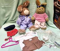 View of both plush bunny rabbits with various clothing and accessories arranged around them on a green surface.