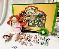Full view of the toy tote, large doll seated in front, and 18 miniature dolls spread out, showcasing contents and scale.
