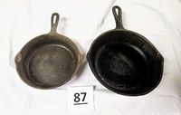 Top view of two vintage cast iron skillets side by side on a white background showing their cooking surfaces and handles.