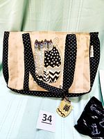 Front view of beige and black zippered tote bag with cat applique detail and signed Laurel Burch cat tag attached