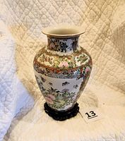 Front view of the Chinese porcelain vase on a carved wooden base, showing colorful floral and bird designs.