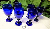 Set of six vintage cobalt blue Libbey stemmed goblet glasses shown grouped together, with a white background and green cloth in background.