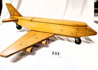Side angle of the wooden cargo airplane showing the full left wing, cockpit area, cargo lid and rear tail fin with logo, standing on its rolling wheels.