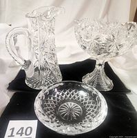 Full set of three American Brilliant Period cut glass pieces on black cloth showing pitcher, compote, and ashtray
