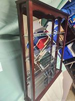 Left angled side view of the wooden display case showing glass shelves and reflective mirror backing.