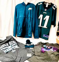 All items displayed on a wall and flat surface, showing hoodie, jersey, knit hat, and both long-sleeve t-shirts