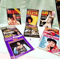 Photo showing seven Elvis magazines arranged on a chair with covers visible, featuring various Elvis themed issues including quiz games and collector magazines.