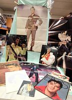 Photo showing multiple Elvis posters and memorabilia including the large signed Army Uniform poster and other Elvis singing posters with newspaper pages and collectibles.
