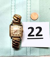 Overall front view of the Gruen Veri-Thin Precision watch with expandable gold tone band and a penny for scale