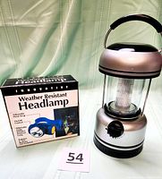 Photo showing Innovative Weather Resistant Headlamp box with illustration of blue headlamp and black carrying strap next to the Guide Gear metallic silver and black lantern with a carrying handle.