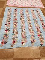 Full view of the quilt laid flat, showing six vertical rows of colorful squares on a light blue background covering the entire surface with visible hand knots.