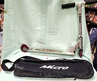 Full view of folded scooter standing against light background with carry case lying in front