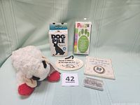 Full lot showing two ceramic dog plaques with sentimental phrases, a box of dog-shaped paper clips, PAWZ dog boots box, Lamb Chop dog toy, and Dog Pile puzzle