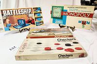 Photo of all four game boxes: Battleship box features children playing, Monopoly box labeled Parker Brothers with game title, Mahjong and Checkers boxes stacked.