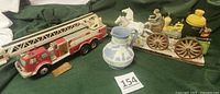 Photo showing all three items on a green cloth background: red and white fire truck decanter with a ladder, blue and white Fireman's Wife pitcher, and a vintage fire engine decanter with figures.