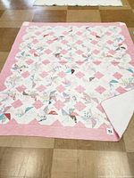 Full view of the vintage pinwheel quilt laid flat on a tiled floor, showing the overall pattern, pink border, and scalloped edge.