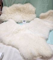 Shows all three white sheep fleece pieces laid out on a light blue chair, highlighting their irregular shapes and soft, fluffy pile.