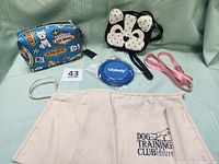 Full set showing blue Marc Tetro dog-themed make-up bag, dog-face-shaped cross-body bag, Chewy collapsible bowl, pink dog leash, beige Dog Training Club apron, two dog print hot pads/pot holders.