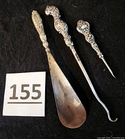 Full set of three silver shoe implements with decorative handles including shoehorn, shoe lacing hook, and cuticle tool.